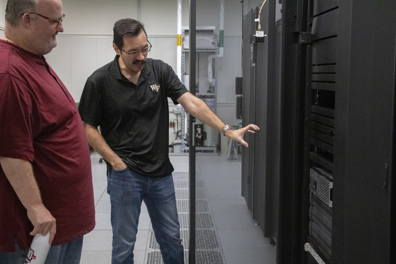 A Wake Forest HPC staff member points toward a server rack.